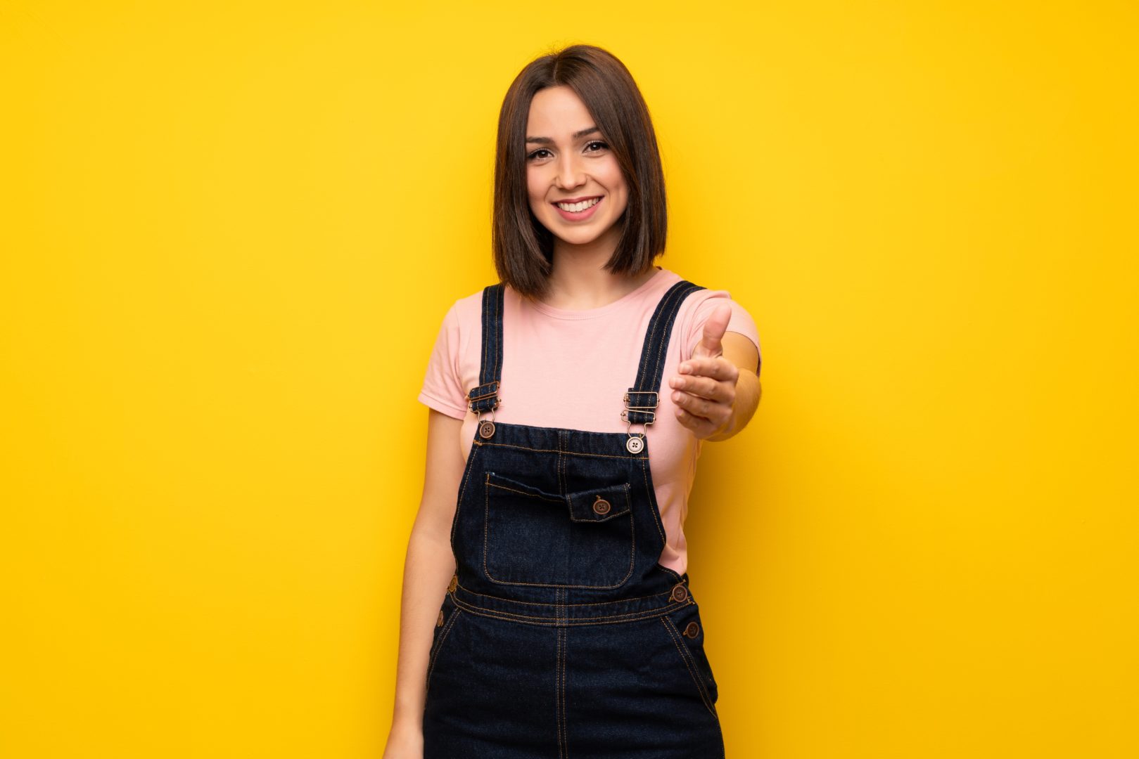 Young woman over yellow wall shaking hands for closing a good deal