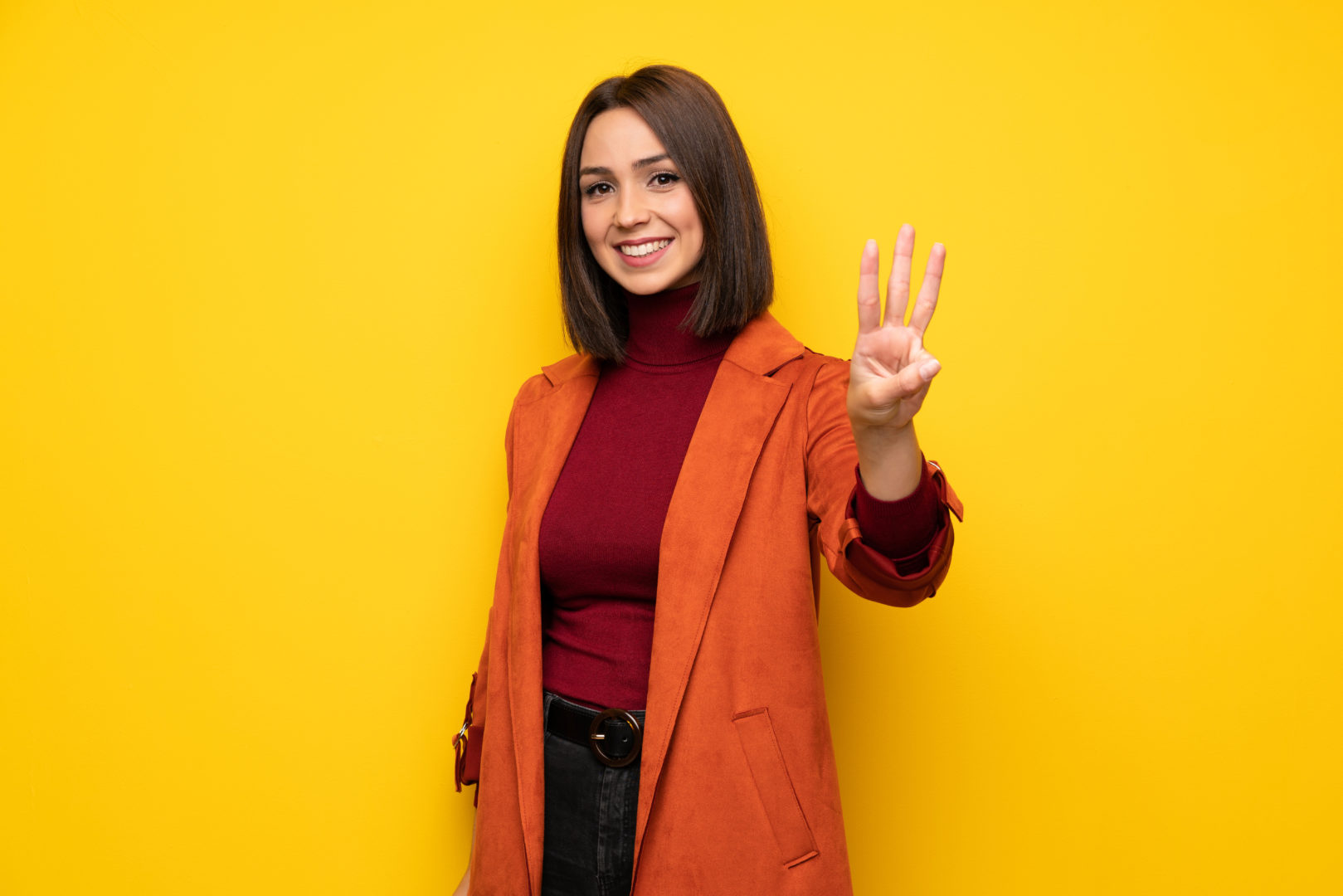 Young woman with coat happy and counting three with fingers